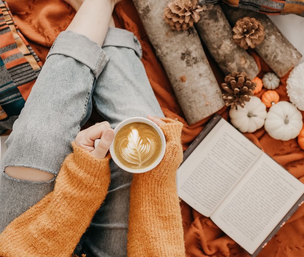 Warm autumn scene with latte art coffee, book, and cozy sweater in an inviting atmosphere.