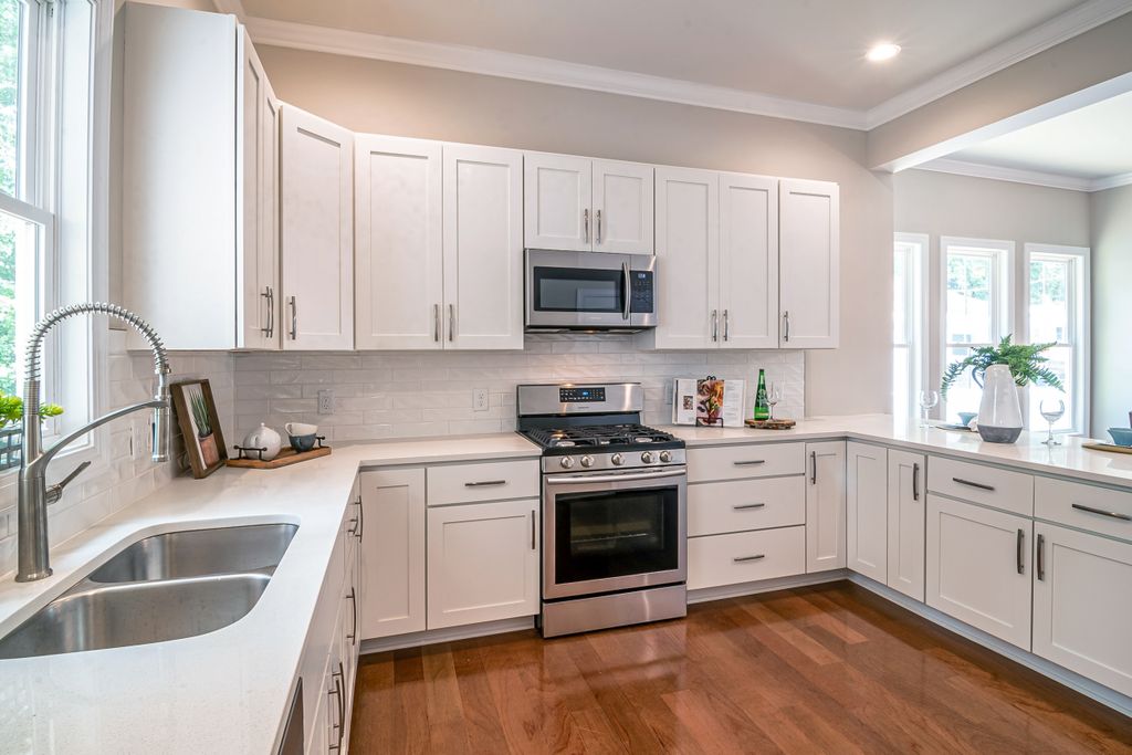 Bright contemporary kitchen featuring white cabinetry, hardwood floor, and stainless steel appliances.